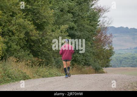 Ein Einzelmann in einem violetten Oberteil, joggt auf einer ungemachten Straße, wandert, Fitness Stockfoto
