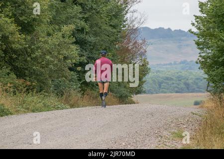 Ein Einzelmann in einem violetten Oberteil, joggt auf einer ungemachten Straße, wandert, Fitness Stockfoto