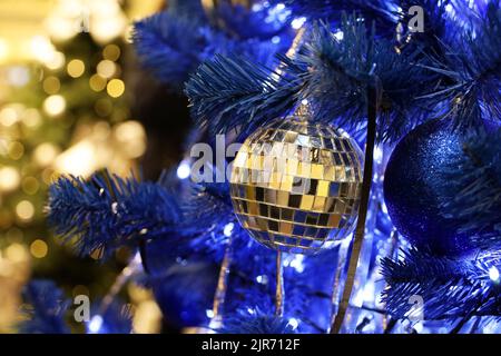 Weihnachtsbaum mit blauen und Spiegelkugeln in einem Einkaufszentrum vor dem Hintergrund verschwommener festlicher Lichter. Neujahr Spielzeug und Dekorationen, Winterferien Stockfoto