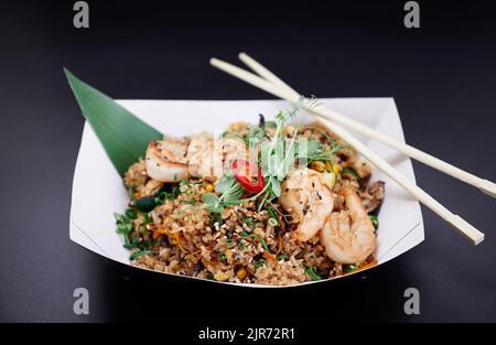 Chinesisches leckeres Fast Food auf Pappteller. Garnelen, Tintenfisch und Tintenfisch mit Reisrührbraten und Gemüse als vegetarisches Speisekonzept. Gebratener Reis mit Meeresfrüchten, zubereitet im Wok. Hochwertige Bilder Stockfoto