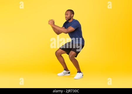 Athletischer Afrikanischer Amerikanischer Mann, Der Deep Squat-Übung Macht, Gelber Hintergrund Stockfoto