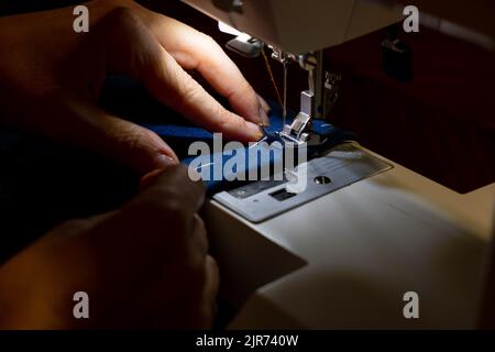 Weibliche Hände eines Schneidermeisters, der mit blauem Gewebe arbeitet Stockfoto