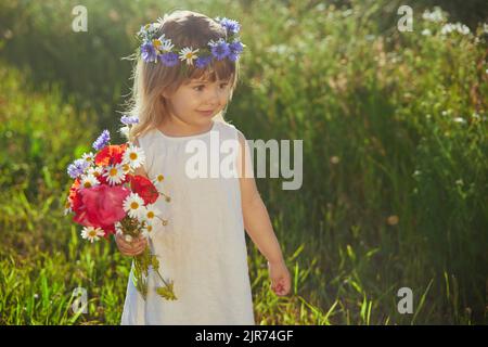 Charmantes Kind in Leinenkleid geht in einem Feld mit Blumen Stockfoto