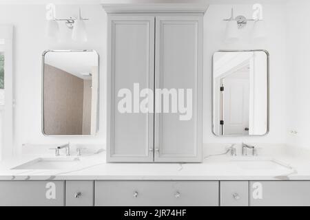 Der graue Schrank im luxuriösen Badezimmer ist mit einer weißen Marmorablagefläche, Chromzapfhähnen und Spiegeln ausgestattet. Stockfoto