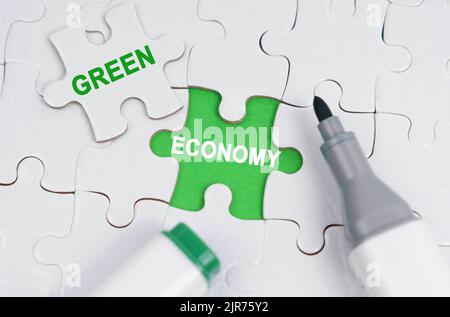 Ökologisches Konzept. Weiße Rätsel liegen auf einem grünen Hintergrund, anstelle eines offenen Puzzles steht geschrieben - Grüne Wirtschaft Stockfoto