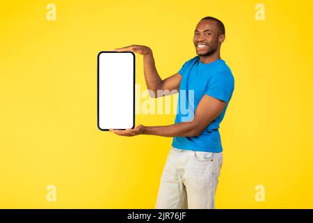 Schwarzer Mann Hält Großes Telefon Mit Leerem Bildschirm, Gelber Hintergrund Stockfoto