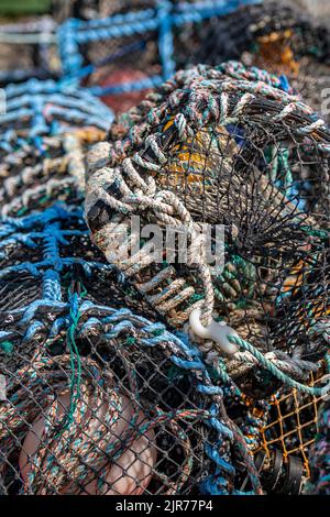 Hummertöpfe und Fischernetze in einer abstrakten Komposition, die am Kai eines Fischereihafens zurückgelassen wurde, farbenfrohe Fischernetze und Fallen mit struktureller Struktur. Stockfoto