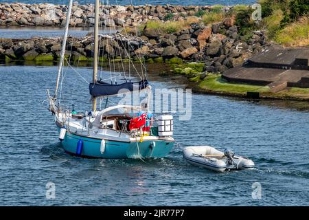 Kleine Yacht mit einem Segler am Steuer, der den Hafen in girvan in ayrshire verlässt und ein kleines Schlauchboot oder einen zarten Segler mit Motor schleppt. Stockfoto