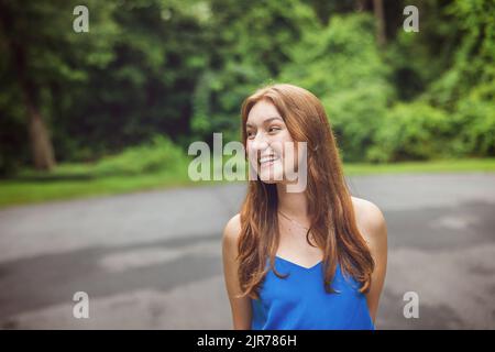 Ein hübsches, rothaariges Teenager-Mädchen, das ein blaues Tanktop trägt und Jeans, die sich auf den Weg zum College machen Stockfoto
