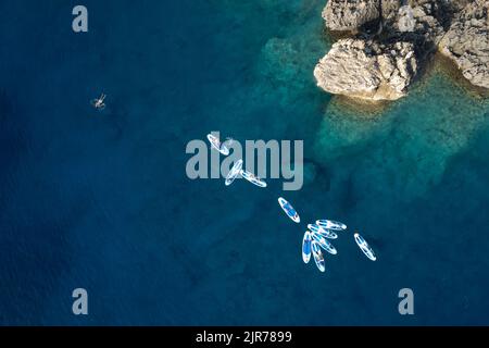 Gruppe von Menschen, die im Meer in der Nähe einer weißen Felsküste Kajakfahren und schwimmen. Stockfoto