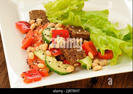 Gemüsesalat mit weißen Bohnen, Roggengeröstungen, Tomaten, Gurken, schwarzen Sesamsamen und Salat in quadratischer Platte, Nahaufnahme horizontal Stockfoto