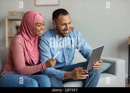 Fröhliche Muslimische Ehegatten, Die Mit Einem Digitalen Tablet Einen Videoanruf Tätigen Und Schwangerschaftsnachrichten Teilen Stockfoto