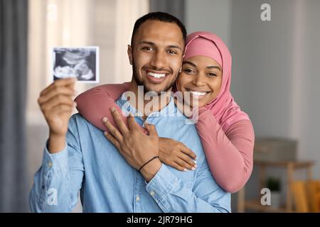 Geburtskonzept. Glückliches schwarzes muslimisches Paar, das ein Baby erwartet und Sonographie vor der Kamera zeigt Stockfoto