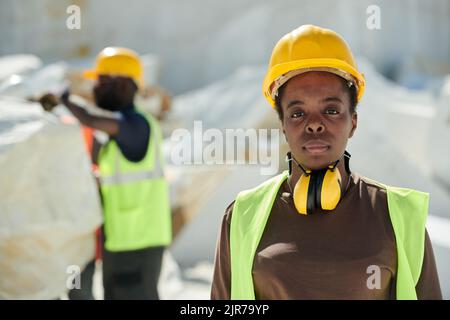 Junge ernsthafte afroamerikanische Arbeiterin aus Marmorbruch in Uniform und Schutzhelm, die im Freien auf die Kamera schaut Stockfoto