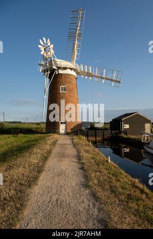 Perspektivischer Blick auf dem Fußweg in Richtung Horsey Wind Pump (Windmühle), einem ikonischen Wahrzeichen von Norfolk Broads in England, Großbritannien. Stockfoto