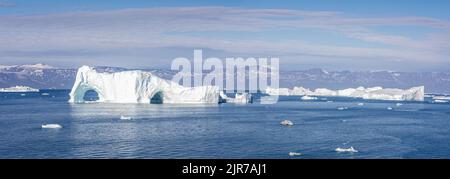 Panorama großer Eisberge mit Bögen, von denen ein Teil in der Disko Bay, Grönland, ins Wasser gefallen ist Stockfoto