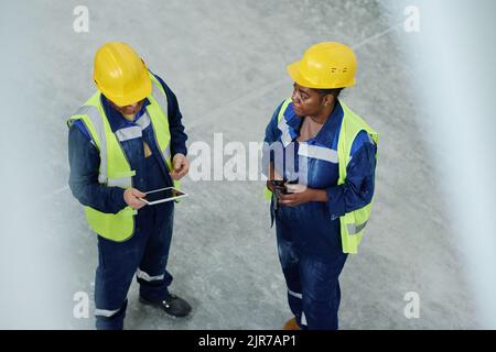 Junger männlicher Ingenieur mit Tablet-Beratungswebsite, um technische Punkte zu spezifizieren, während er während der Diskussion vor einer Kollegin stand Stockfoto