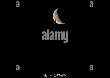 Wunderschöner Viertelmond über der Altstadt von Riga hinter der Domes-Domuhr. Stockfoto