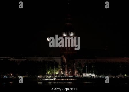 Wunderschöner Viertelmond über der Altstadt von Riga hinter der Domes-Domuhr. Stockfoto