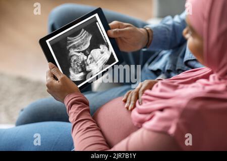 Schwanger schwarz islamischen Paar hält digitale Tablette mit Baby-Ultraschall-Bild Stockfoto