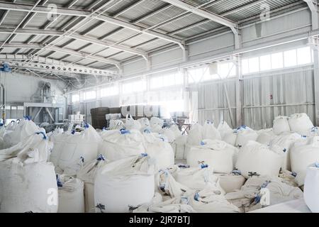 Teil eines geräumigen Lagerhauses oder Lagerraums mit Haufen riesiger weißer Säcke, die lose Rohstoffe für die industrielle Produktion enthalten Stockfoto