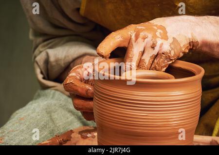Ein Mann in alten mittelalterlichen byzantinischen Kleidern sitzt hinter einem alten Töpferrad und macht Geschirr aus Lehm. Keramik in der Natur im Retro-Stil. Stockfoto