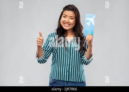Glückliche asiatische Frau mit Flugticket zeigt Daumen nach oben Stockfoto