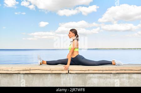 Junge Frau, die sich am Meer komplett aufteilt Stockfoto