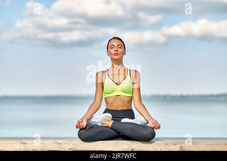 Junge Frau, die am Meer in Lotushaltung meditiert Stockfoto