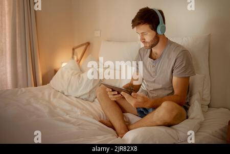 Kopfhörer, digitales Tablet und im Bett, um nachts Online-Filme, Videos oder Serien im Schlafzimmer zu sehen. Mann bei Unterhaltungsnachrichten oder Internetfilmen Stockfoto