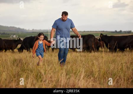 Landwirt Vater, Kind oder Familie mit Kühen auf einem Bauernhof, Grasfeld oder auf dem Land. Nachhaltigkeit oder Umwelt Vater und Mädchen mit Rindern im Hintergrund Stockfoto