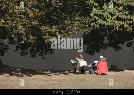 Bild eines älteren Ehepaares, das zusammen vor dem See bohinj liest, während eines Urlaubs, entspannt, im Sommer. Stockfoto