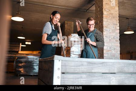 Arbeiter in der Weinherstellung, Produktion und im Keller halten Presswerkzeug, um den Tank für den Alkoholprozess zu zerkleinern, zu mischen und zu rühren. Winzer, Fabrik und Weingut Stockfoto