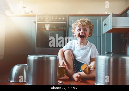 Heute stellte er sich vor, Schlagzeuger zu sein. Portrait eines entzückenden kleinen Jungen, der in der Küche mit Töpfen spielt. Stockfoto