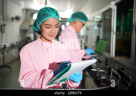 Asiatische Arbeiter arbeiten in Lebensmittel-und Getränke-Industrie-Fabrik mit Hygiene Arbeit Fruchtsaft Produktionslinie Inspektor Personal. Beve Prüfen Stockfoto