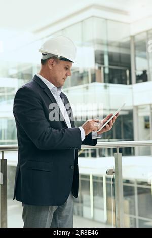Es ist wichtig, die Kosten des Gebäudes im Auge zu behalten. Ein fokussierter professioneller männlicher Architekt, der neben einem Entwicklungsstandort steht, während er ein verwendet Stockfoto