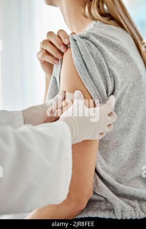 Covid, Impfstoff und Arzt, der den Patienten nach einer medizinischen Behandlung während einer Pandemie mit Gips behandelte. Nahaufnahme des Pflegearbeiters, der sich aufsetzt Stockfoto
