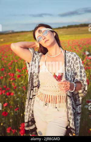 Eine Frau, die bei Sonnenuntergang Erdbeeren auf einem Mohnfeld isst. Vertikales Foto. Stockfoto