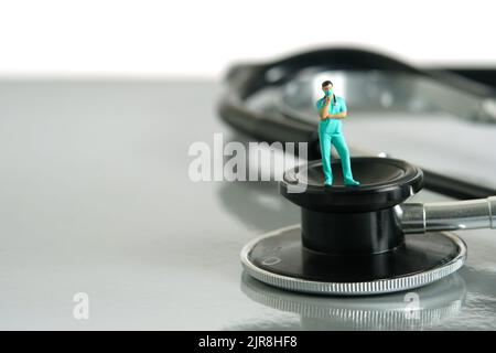 Miniatur Menschen Spielzeug Figur Fotografie. Ein Arzt oder eine Krankenschwester, der über dem Stethoskop auf einem Schreibtisch steht und denkt. Bildfoto Stockfoto