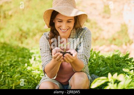 Ein glücklicher junger Bauer hält einen Erdhaufen mit einem Keimling, der draußen aus ihm wächst. Stockfoto