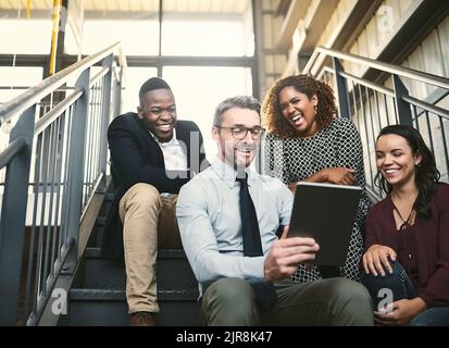 Die Treppe ist ihr WLAN-Hotspot. Eine vielfältige Gruppe von Kollegen, die ein spontanes Treffen mit einem Tablet auf der Treppe haben. Stockfoto