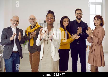 Porträt einer Gruppe von multiethnischen Geschäftsleuten, die applaudieren und stolz lächeln und die Kamera betrachten. Stockfoto
