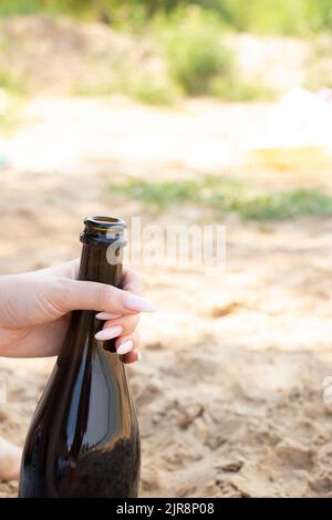 Eine weibliche Hand hält im Sommer am Strand im Urlaub eine Flasche Sekt, eine Flasche Champagner Stockfoto