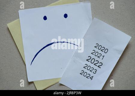 2020 2021 2022 2023 als Liste auf Schecks gedruckt, Neujahr 2022 auf Papier als Hintergrund, eine Liste über die Jahre und ein trauriges Emoticon auf einer Karte gezeichnet, cri Stockfoto