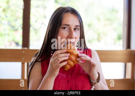 Junge schöne Frau, die Croissant isst Stockfoto