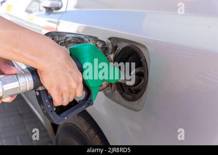 Die Hand einer Frau hält eine Tankpistole in den Hals des Panzers des Autos Stockfoto