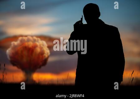 Das Konzept eines Atomstreiks. Silhouette eines Mannes, der am Telefon anruft und den Befehl zum Explodieren gibt. Ein Politiker, der einen Atomkrieg begann Stockfoto