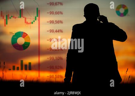 Die Silhouette einer Person - ein Investor, ein Geschäftsmann, ein Händler, der am Telefon anruft und sich das fallende Diagramm der Börse anschaut Stockfoto