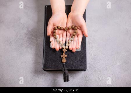 Kinderhände, die das Holzkreuz und die Perlen in Herzform auf der Biblia halten. christianity-Konzept Stockfoto