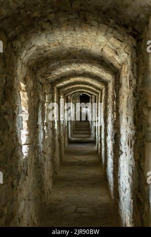 Ein langer Steintunnelgang mit Fenstern in einem alten Schloss. Selektiver Fokus. Stockfoto